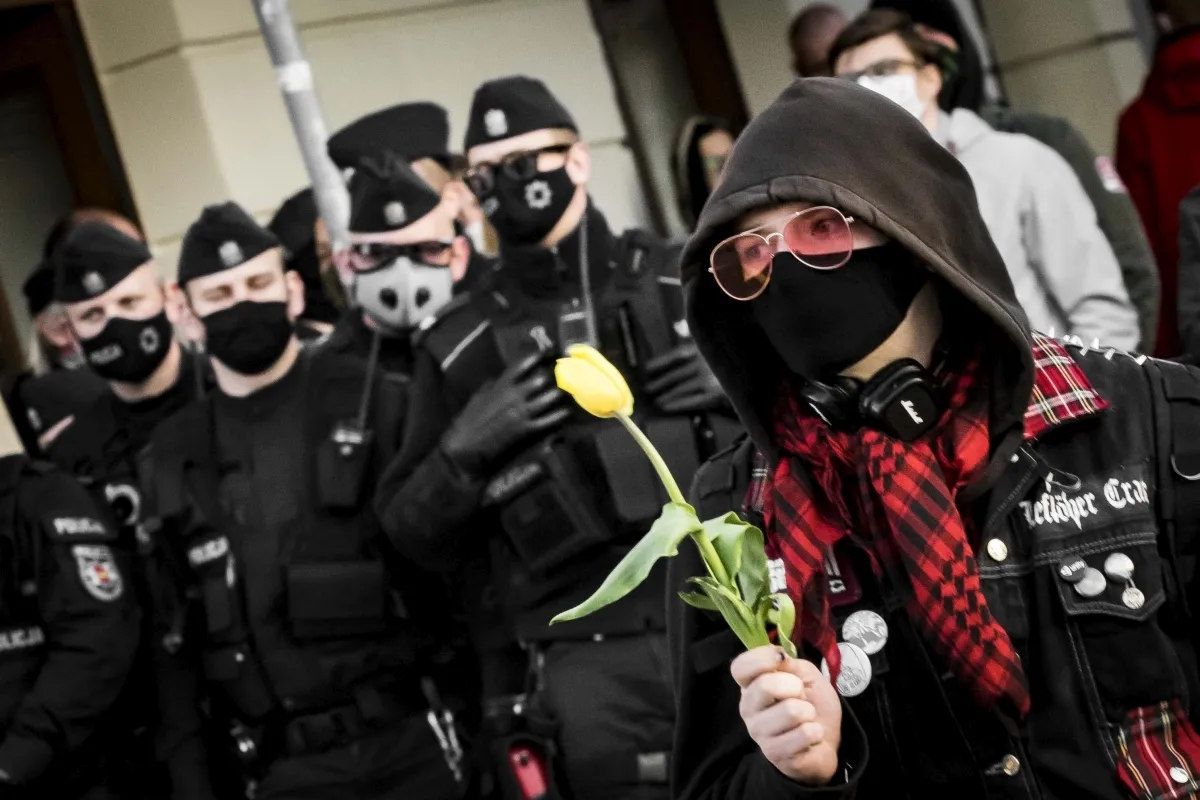 Masked protester holding a yellow tulip in front of police officers